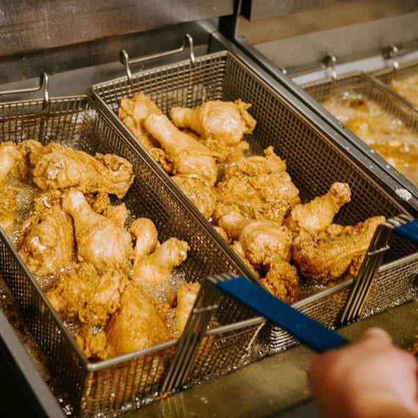 Crispy fried chicken pieces cooking in two deep fryers at Xingones Cantina.