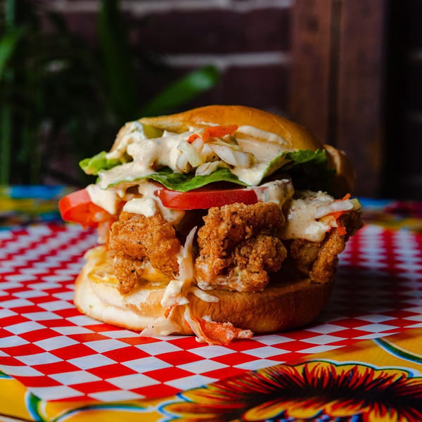 Crispy fried chicken sandwich with lettuce, tomato, and creamy sauce on a red and white checkered paper.