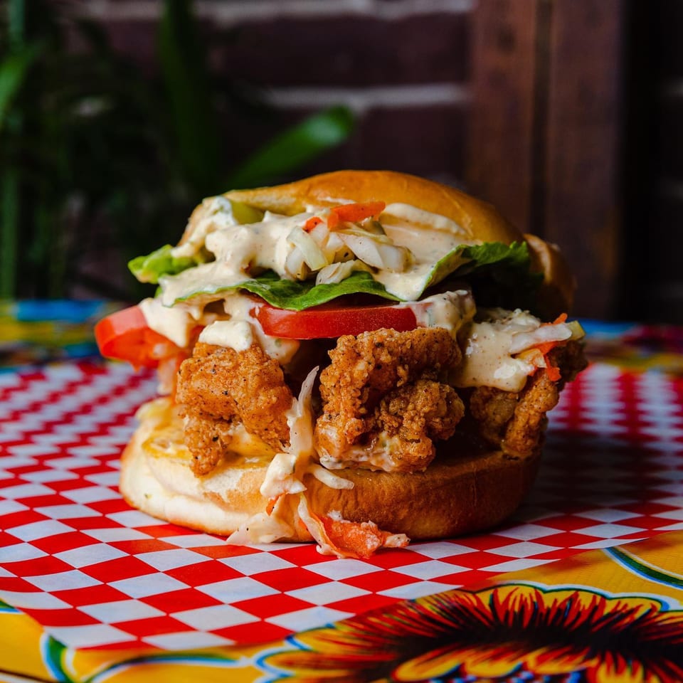 Crispy fried chicken sandwich with lettuce, tomato, and creamy sauce on a red and white checkered paper.