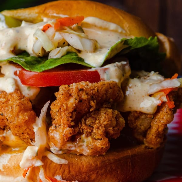 Close-up of a fried shrimp burger with lettuce, tomato, and creamy sauce on a brioche bun.