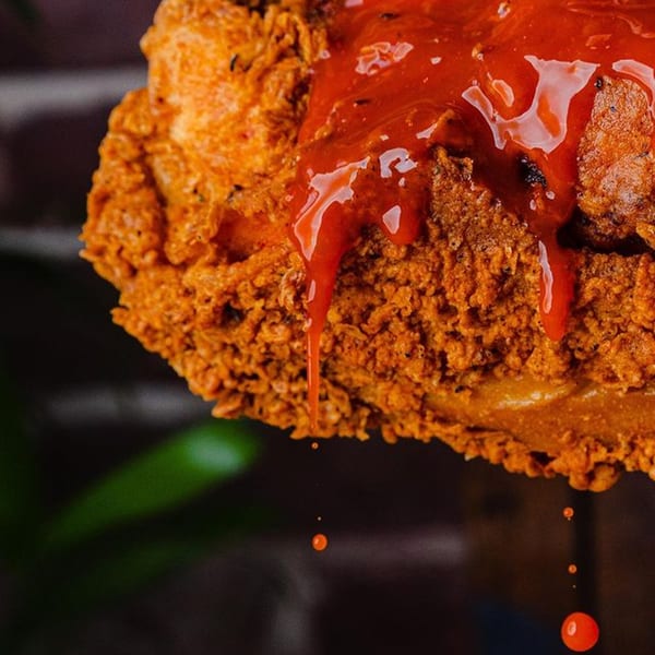 Crispy fried chicken, generously drizzled with a vibrant red sauce, with sauce dripping down.