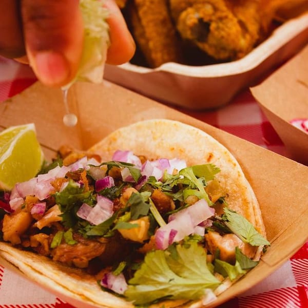 A hand squeezes lime over a Xingones Cantina taco with meat, onions, and cilantro.