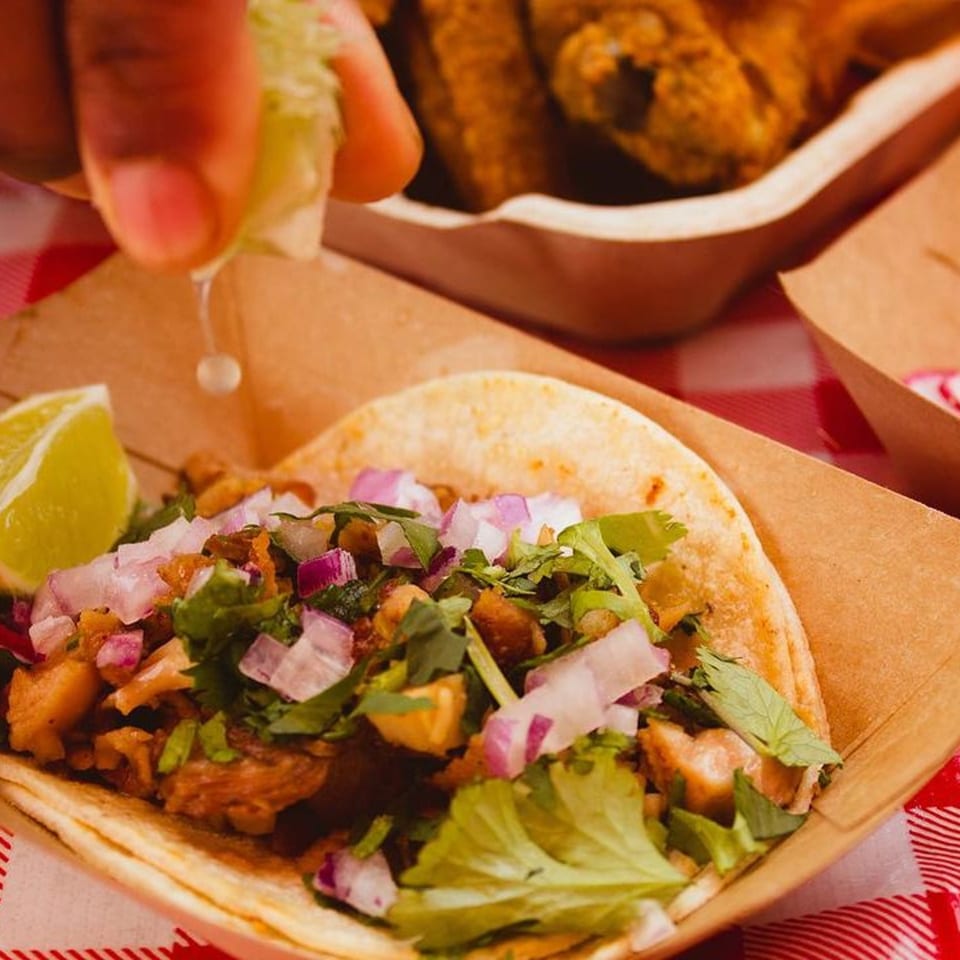 A hand squeezes lime over a Xingones Cantina taco with meat, onions, and cilantro.