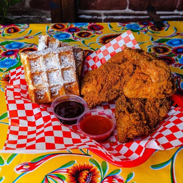 Crispy fried chicken and powdered sugar waffles with dipping sauces on a vibrant floral tablecloth.