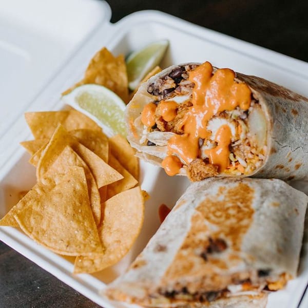 Two burritos with orange sauce and a side of tortilla chips and lime wedges in a white container.