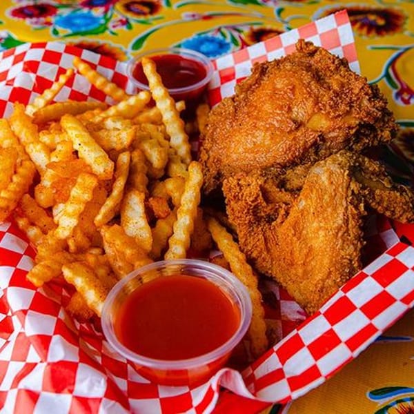 Crispy fried chicken and crinkle-cut fries with two cups of red sauce in a red and white checkered basket.